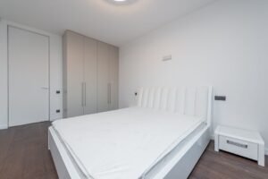 Bare mattress on a bed frame in a bright bedroom, ready for a mattress topper