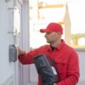 Delivery person ringing a smart video doorbell while holding a package