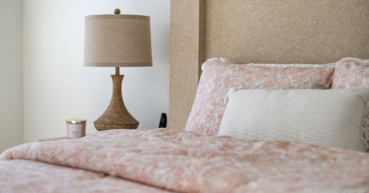 A bed layered with soft pink floral bedding beside a table lamp