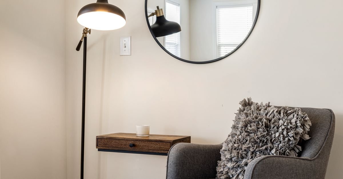 A round mirror and floor lamp beside a grey armchair