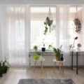 A bright rental apartment living room with plants, sheer curtains and a leaning mirror