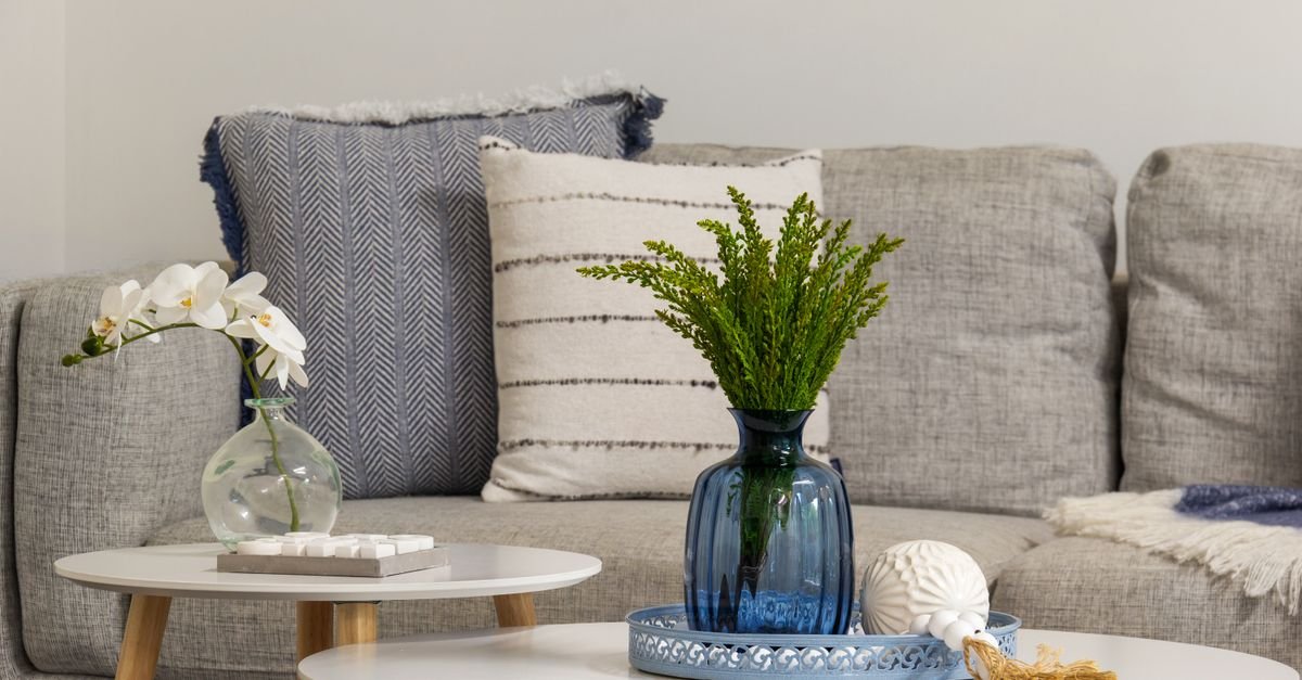 Round nesting coffee tables styled with a vase and greenery beside a grey sofa