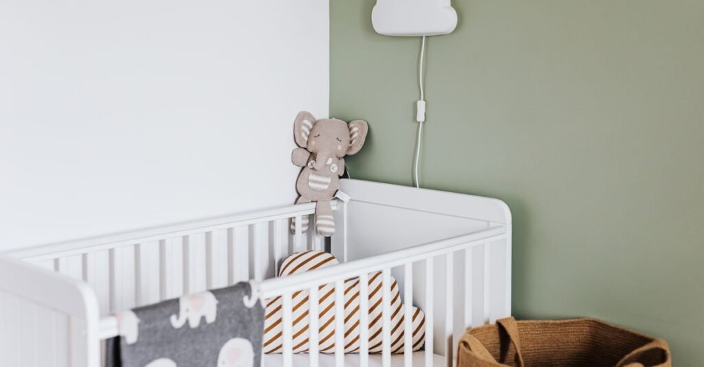 White crib in a sage nursery with a cloud lamp
