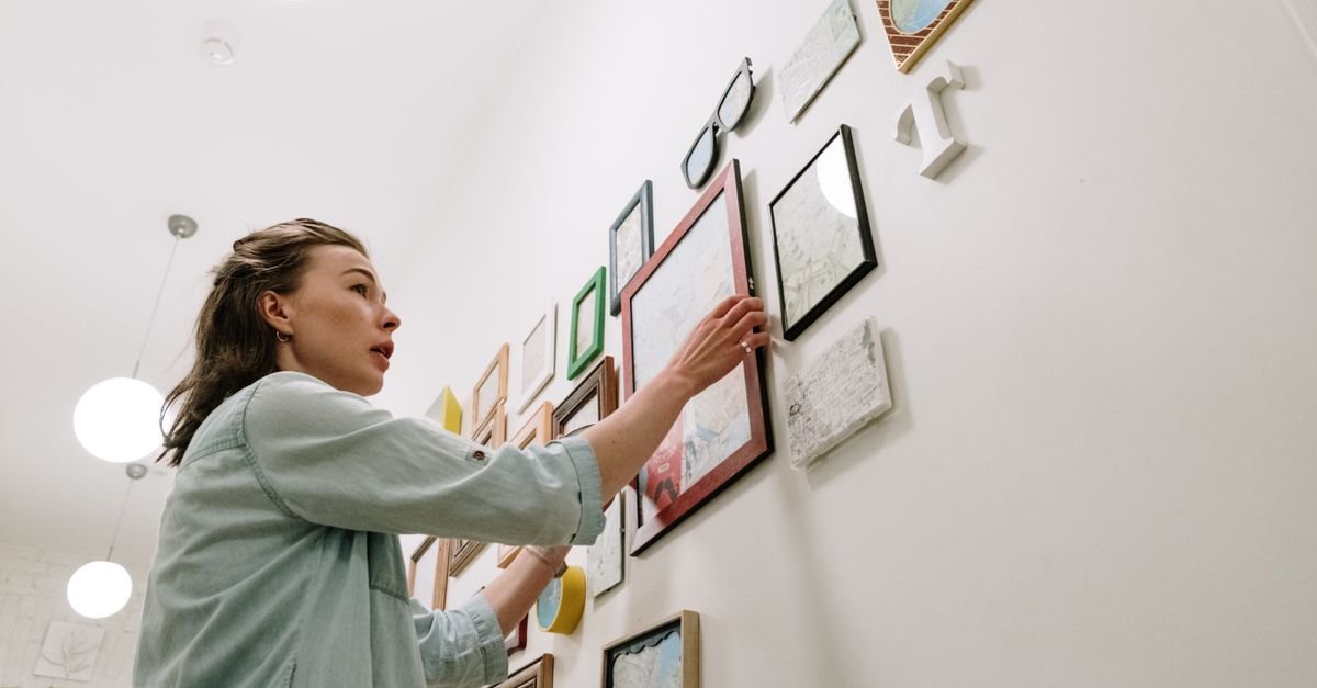 A woman arranging framed pictures into a gallery wall