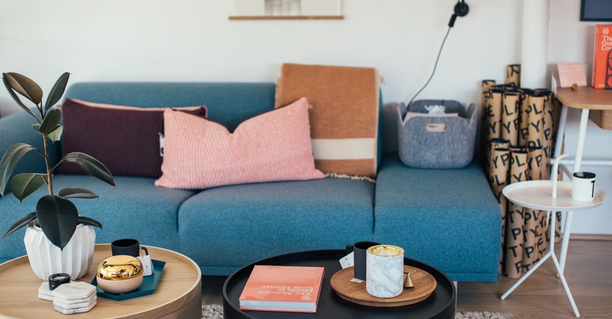 A styled living room with a blue sofa and round coffee tables holding books and candles
