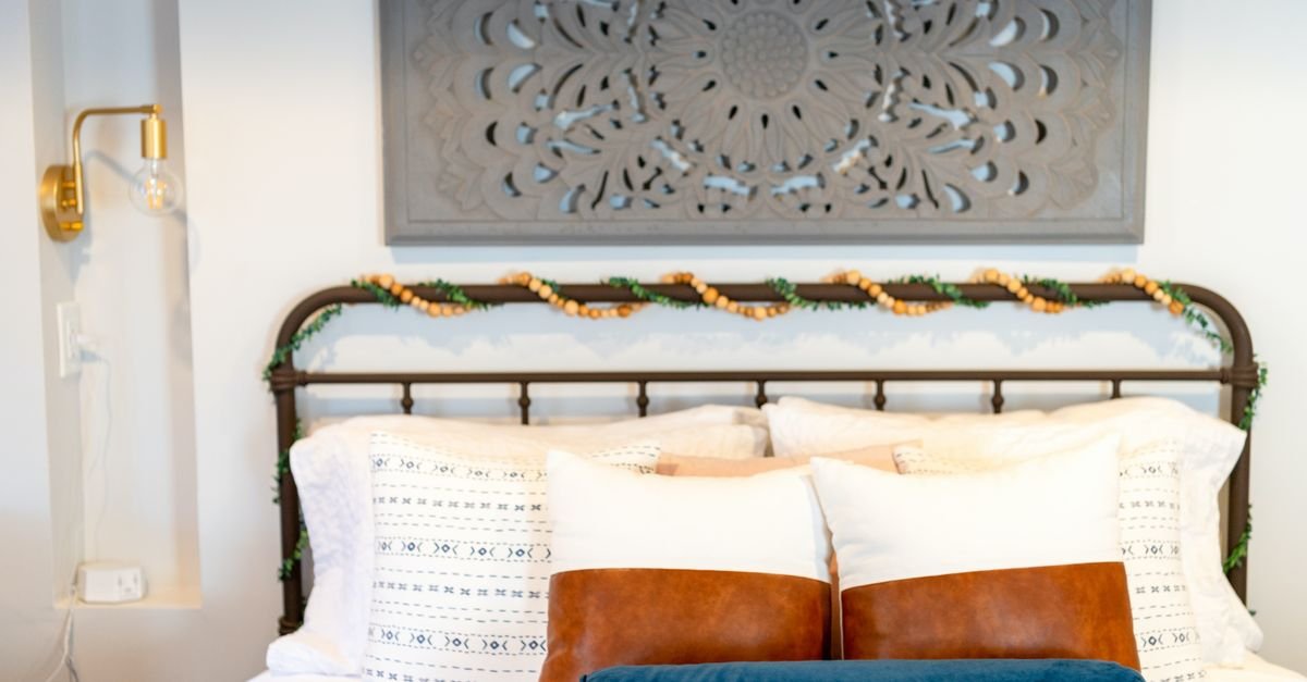 A designer bed with black iron frame, layered white bedding and leather and blue pillows