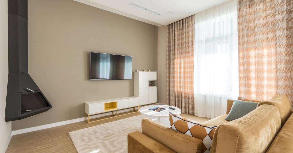 A living room with curtains hung high beside a TV wall