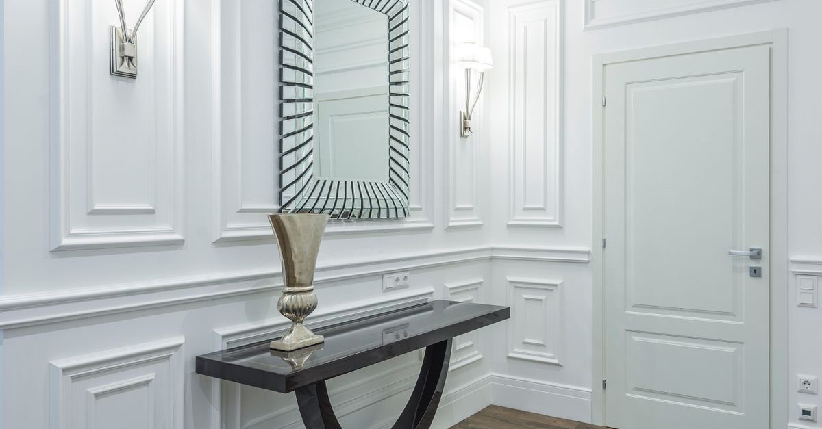 An elegant entryway with a dark console table and patterned mirror on panel molding