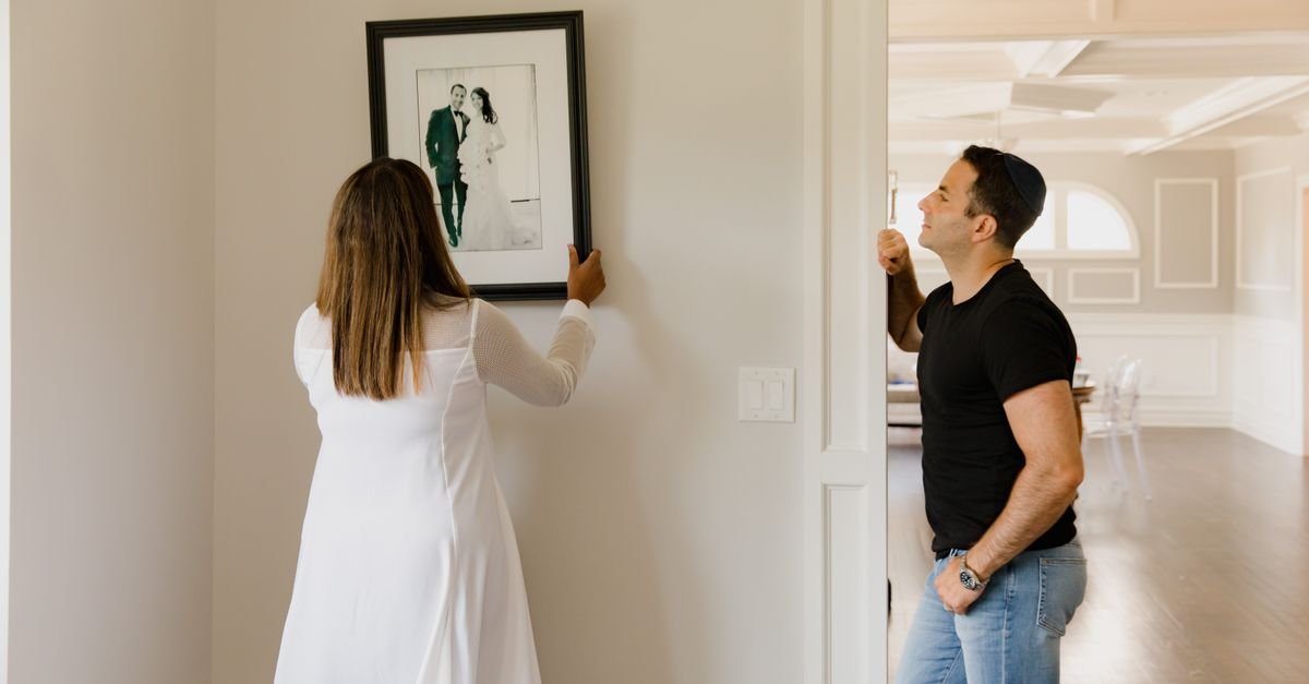 A couple hanging a framed artwork on a wall