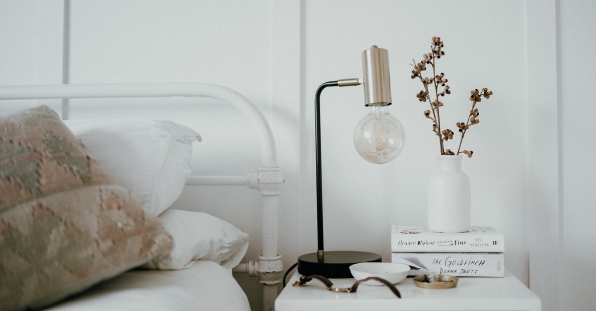 A white nightstand with a modern lamp, book and glasses