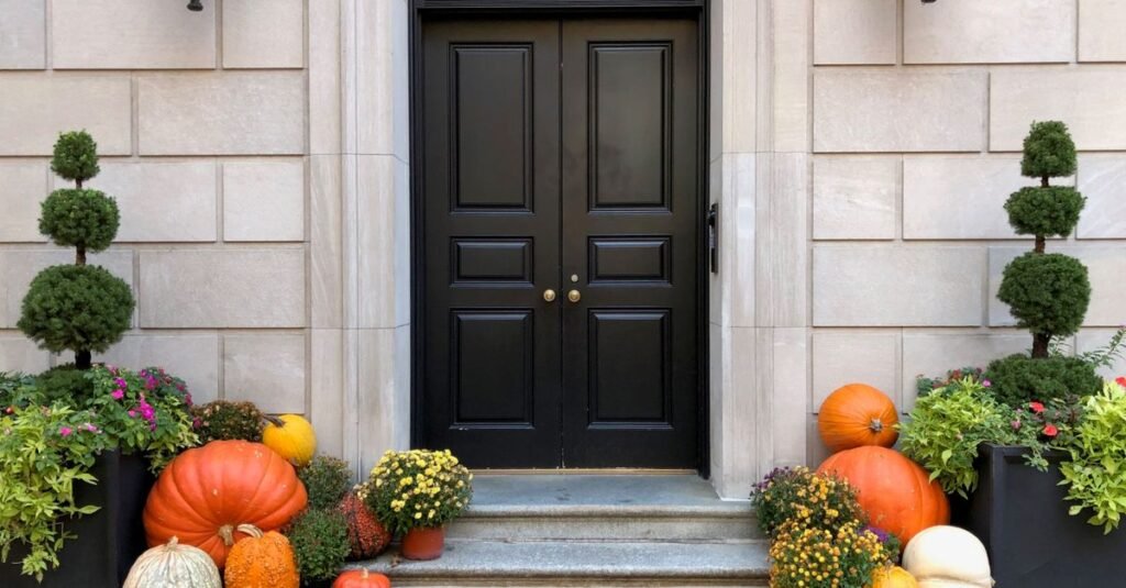 Black door with pumpkins and topiaries on the steps
