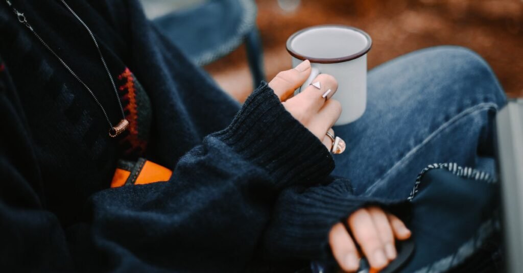 Hands around a warm mug in a cozy sweater outdoors
